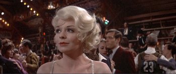 Movie still from “They Shoot Horses, Don't They?” (1969), directed by Sydney Pollack – A woman with blonde hair is standing in front of a group of people; Close Up shot, Over the shoulder angle
