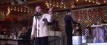 Movie still from “They Shoot Horses, Don't They?” (1969), directed by Sydney Pollack – An older man giving a peace sign at an event; Medium shot, Over the shoulder angle