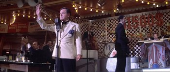 Movie still from “They Shoot Horses, Don't They?” (1969), directed by Sydney Pollack – An older man singing into a microphone in front of a crowd; Medium shot, Over the shoulder angle