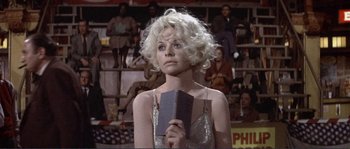 Movie still from “They Shoot Horses, Don't They?” (1969), directed by Sydney Pollack – A woman holding a book in front of a group of people; Close Up shot, Low angle