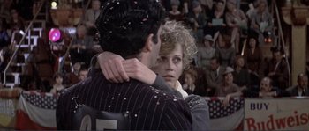Movie still from “They Shoot Horses, Don't They?” (1969), directed by Sydney Pollack – A man and a woman embracing in front of a crowd; Medium shot, Low angle