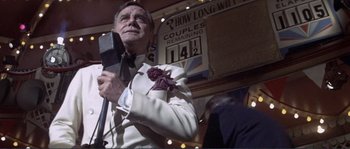 Movie still from “They Shoot Horses, Don't They?” (1969), directed by Sydney Pollack – An older man holding a microphone in front of a crowd of onlookers; Medium shot, Low angle