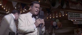 Movie still from “They Shoot Horses, Don't They?” (1969), directed by Sydney Pollack – An older man in a white suit is holding a microphone; Medium shot, Low angle