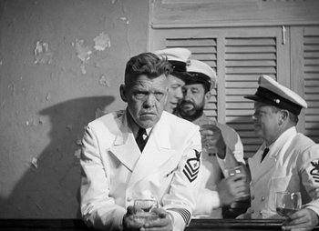 Movie still from “They Were Expendable” (1945), directed by Robert Montgomery – An old photo of a man in a uniform holding a drink; Medium shot, Over the shoulder angle