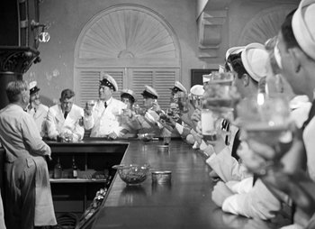 Movie still from “They Were Expendable” (1945), directed by Robert Montgomery – A group of men sitting at a table with food; Wide shot, High angle