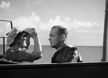 Movie still from “They Were Expendable” (1945), directed by Robert Montgomery – A man looking at another man with binoculars in front of a body of water; Medium shot, Over the shoulder angle