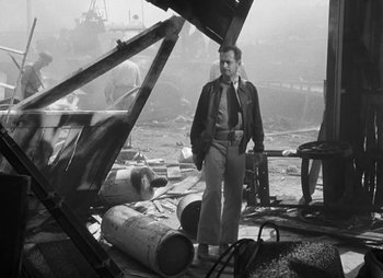 Movie still from “They Were Expendable” (1945), directed by Robert Montgomery – A man standing next to a pile of barrels; Wide shot, Low angle