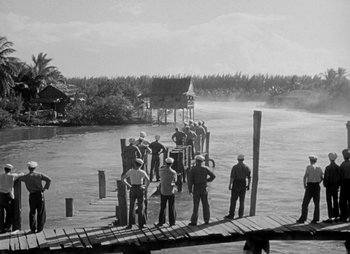 Movie still from “They Were Expendable” (1945), directed by Robert Montgomery – A black and white photo of a group of men standing on a pier; Extreme Wide shot, High angle