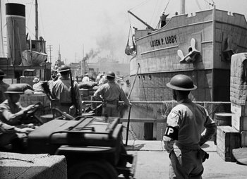 Movie still from “They Were Expendable” (1945), directed by Robert Montgomery – A group of men standing next to each other near a boat; Wide shot, Over the shoulder angle