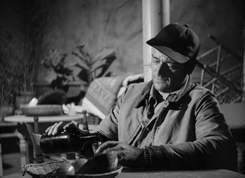 Movie still from “They Were Expendable” (1945), directed by Robert Montgomery – An older man sitting at a table with a bottle of wine; Medium shot, High angle