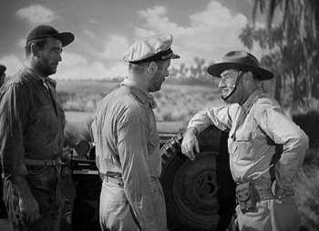 Movie still from “They Were Expendable” (1945), directed by Robert Montgomery – A group of men standing next to each other near trees; Medium shot, Over the shoulder angle