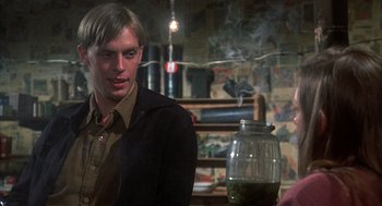 Movie still from “Thieves Like Us” (1974), directed by Robert Altman – A man sitting in front of a glass jar in a room; Medium shot, Over the shoulder angle