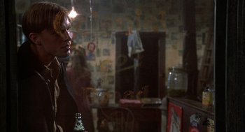 Movie still from “Thieves Like Us” (1974), directed by Robert Altman – A man standing in a living room holding a bottle; Medium shot, Over the shoulder angle