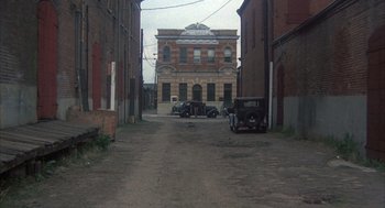Movie still from “Thieves Like Us” (1974), directed by Robert Altman – An old car parked in an alley with a brick building in the background; Extreme Wide shot, High angle