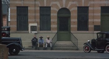 Movie still from “Thieves Like Us” (1974), directed by Robert Altman – A group of men sitting on the steps of a building; Extreme Wide shot, High angle
