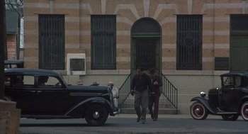 Movie still from “Thieves Like Us” (1974), directed by Robert Altman – Two men walking down the street in front of a building; Wide shot, High angle
