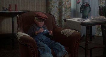 Movie still from “Thieves Like Us” (1974), directed by Robert Altman – A young boy sitting in a chair with a hat on; Medium shot, High angle