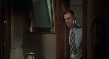 Movie still from “Thieves Like Us” (1974), directed by Robert Altman – A man in a tie leaning against a wall; Medium shot, Over the shoulder angle