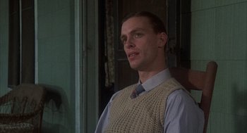 Movie still from “Thieves Like Us” (1974), directed by Robert Altman – A man wearing a sweater vest standing in front of a window; Close Up shot, Low angle