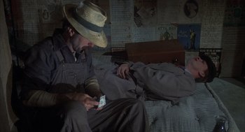 Movie still from “Thieves Like Us” (1974), directed by Robert Altman – A man sitting on a bed looking at his cell phone; Medium shot, High angle