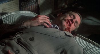 Movie still from “Thieves Like Us” (1974), directed by Robert Altman – A man in a gray suit is laying on the ground with blood all over his face; Close Up shot, High angle