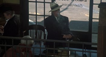 Movie still from “Thieves Like Us” (1974), directed by Robert Altman – A man in a suit and hat sitting at a table; Wide shot, High angle