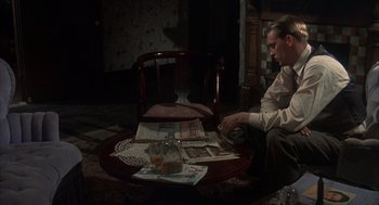 Movie still from “Thieves Like Us” (1974), directed by Robert Altman – A man sitting at a table looking at newspapers; Medium shot, High angle