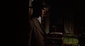 Movie still from “Thieves Like Us” (1974), directed by Robert Altman – A man wearing a suit and a hat standing next to suitcases; Medium shot, Low angle