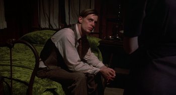 Movie still from “Thieves Like Us” (1974), directed by Robert Altman – A man sitting on top of a couch in a room; Medium shot, High angle