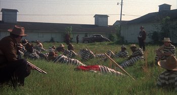 Movie still from “Thieves Like Us” (1974), directed by Robert Altman – A group of men in striped vests laying in the grass; Extreme Wide shot, High angle