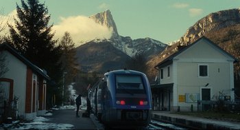 A train on a track near a building with a mountain in the background
