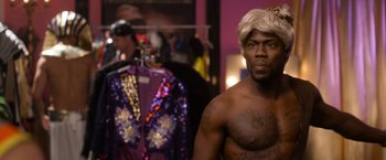 Movie still from “Think Like a Man Too” (2014), directed by Tim Story – A man with a blonde wig and a tattoo on his chest; Medium shot, Over the shoulder angle