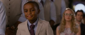 Movie still from “Think Like a Man Too” (2014), directed by Tim Story – A boy in a suit and tie smiling for the camera; Close Up shot, Over the shoulder angle