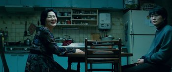 Movie still from “Thirst” (2009), directed by Park Chan-wook – A woman sitting at a table in a kitchen; Medium shot, Low angle