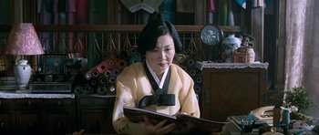 Movie still from “Thirst” (2009), directed by Park Chan-wook – A woman in a yellow and black outfit looking at a book; Medium shot, Low angle