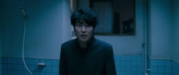 Movie still from “Thirst” (2009), directed by Park Chan-wook – A man in a black jacket standing next to a blue tiled wall; Medium shot, Low angle