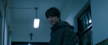 Movie still from “Thirst” (2009), directed by Park Chan-wook – A man in a robe standing next to a cross; Close Up shot, Low angle
