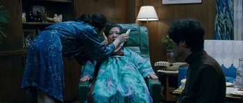 Movie still from “Thirst” (2009), directed by Park Chan-wook – An older woman is sitting in a chair while a younger woman examines her face; Medium shot, High angle