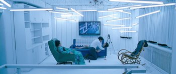 Movie still from “Thirst” (2009), directed by Park Chan-wook – Two men and a woman are sitting on a blue couch in front of a television; Wide shot, Overhead angle