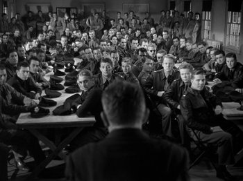 Movie still from “Thirty Seconds Over Tokyo” (1944), directed by Mervyn LeRoy – A group of men sitting in front of a man in front of a table; Wide shot, Over the shoulder angle
