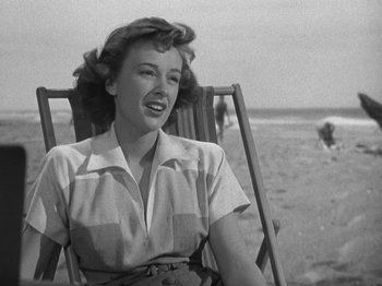 Movie still from “Thirty Seconds Over Tokyo” (1944), directed by Mervyn LeRoy – A woman sitting in a chair on the beach; Medium shot, Low angle