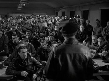 Movie still from “Thirty Seconds Over Tokyo” (1944), directed by Mervyn LeRoy – A group of men sitting in front of a man in uniform; Wide shot, High angle