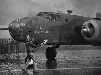 Movie still from “Thirty Seconds Over Tokyo” (1944), directed by Mervyn LeRoy – An old photo of a man standing next to an airplane; Wide shot, Low angle