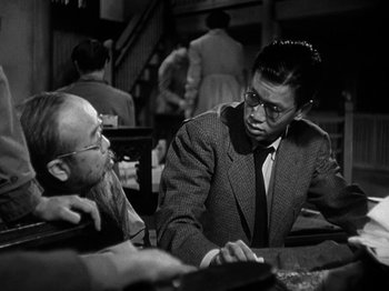 Movie still from “Thirty Seconds Over Tokyo” (1944), directed by Mervyn LeRoy – A man in a suit talks to another man in a suit; Medium shot, Over the shoulder angle