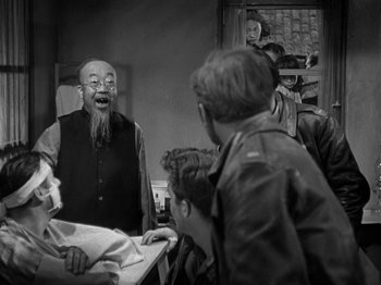 Movie still from “Thirty Seconds Over Tokyo” (1944), directed by Mervyn LeRoy – An old man is talking to a group of people; Medium shot, Over the shoulder angle