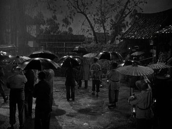 Movie still from “Thirty Seconds Over Tokyo” (1944), directed by Mervyn LeRoy – A black and white photo of people holding umbrellas; Extreme Wide shot, High angle