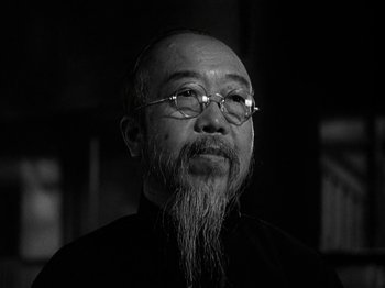 Movie still from “Thirty Seconds Over Tokyo” (1944), directed by Mervyn LeRoy – A man with a beard and glasses is looking at the camera; Close Up shot, Low angle