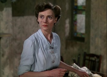 Movie still from “This Happy Breed” (1944), directed by David Lean – An older woman in a blue dress is standing in front of a table; Close Up shot, Low angle