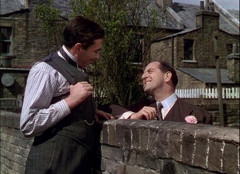 Movie still from “This Happy Breed” (1944), directed by David Lean – Two men talking to each other while standing next to a brick wall; Medium shot, Over the shoulder angle