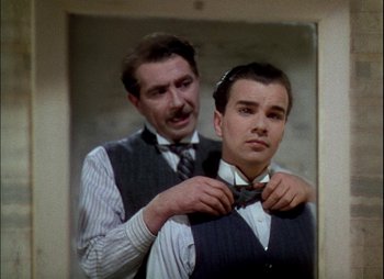 Movie still from “This Happy Breed” (1944), directed by David Lean – A man helping another man put on a bow tie; Medium shot, Over the shoulder angle